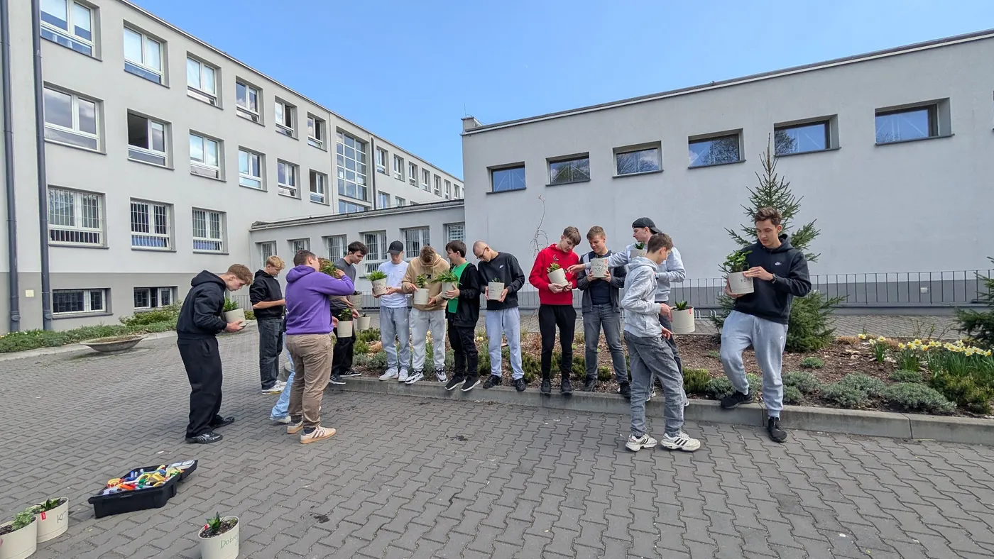 Uczniowie sadzą rośliny w donicach na dziedzińcu szkoły podczas warsztatu naprawczego, 2026